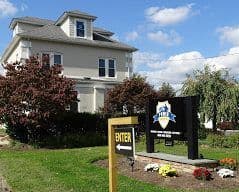 A white colonial home with the Power Construction sign at the end of the drive