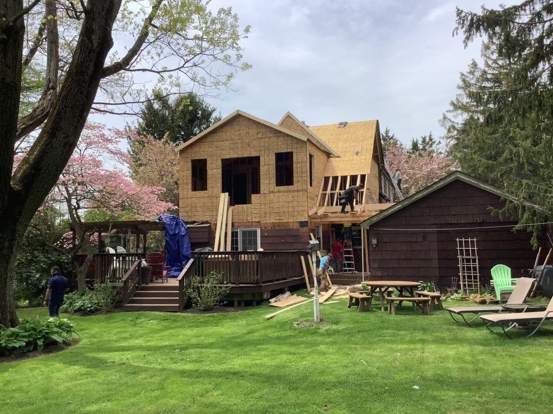 A home addition under construction in a back garden, framed and sheathed with the deck alongside