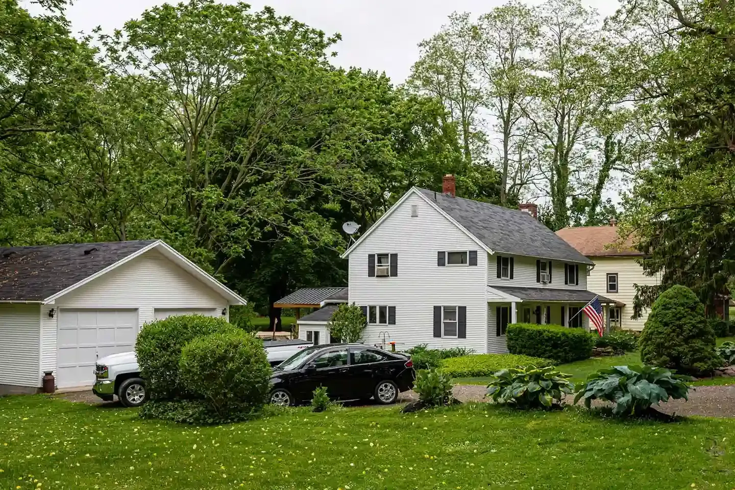 A white farmhouse with an attached garage set among mature trees